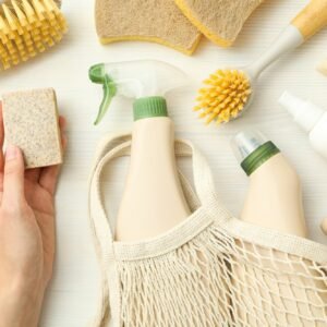 Eco bag, hand, bottles with detergents and cleaning tools on light background, top view